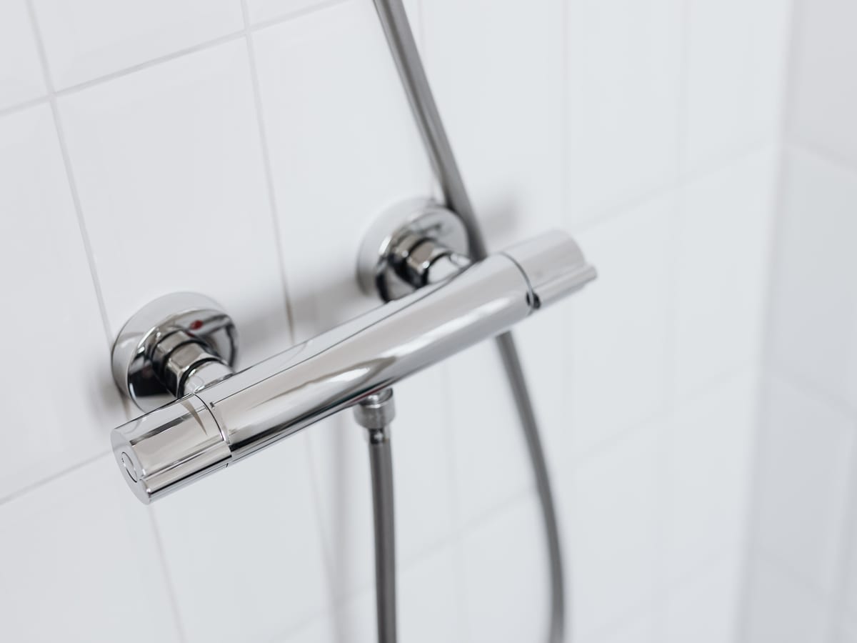 Modern chrome shower faucet on white tiled wall, elegant and clean design.