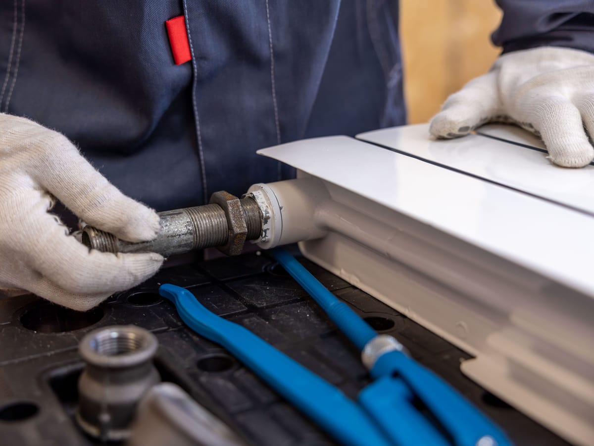 Close-up of a plumber installing a radiator pipe using specialized tools.