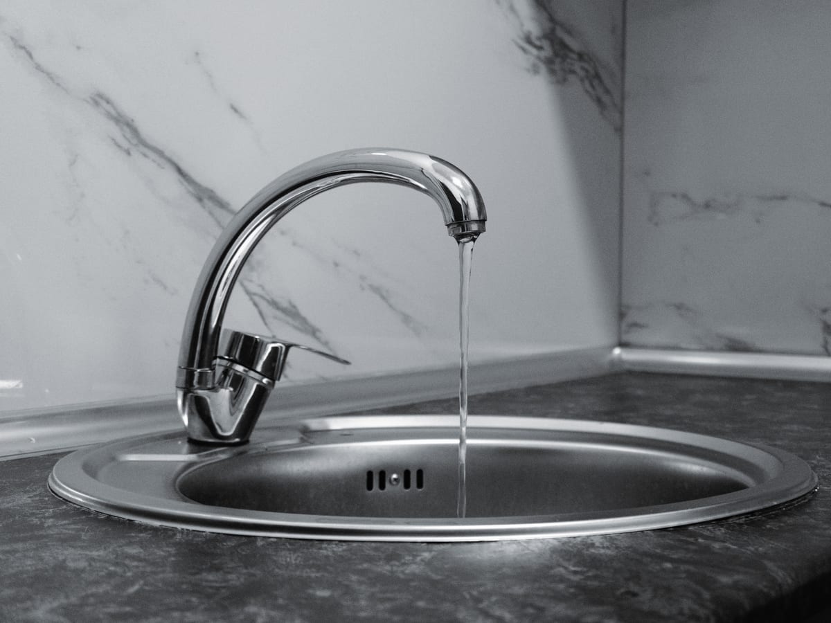 Chrome faucet with running water in a modern kitchen with marble countertop.